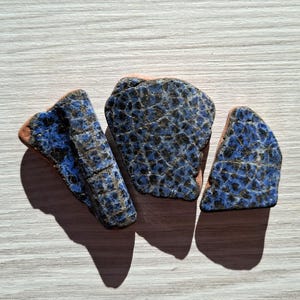 May include: Three pieces of blue and black ceramic pottery with a crackled glaze. The pieces are irregular in shape and have a rough texture.