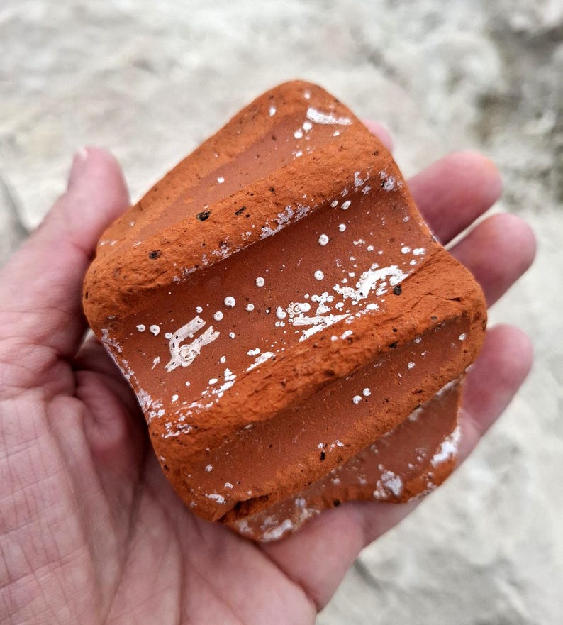 May include: A close-up of a red clay brick with white markings. The brick has a rough, textured surface and is slightly curved.