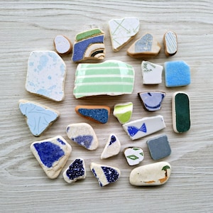 May include: A collection of colorful, broken ceramic tiles with blue, green, white, and brown patterns. The tiles are arranged in a circle on a light wood surface.