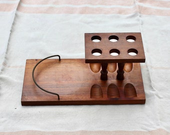 May include: A wooden egg holder with a tray. The holder has 9 holes and 4 small indentations. The tray has a metal handle.