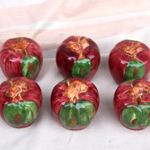 May include: Set of six ceramic apple salt and pepper shakers. The shakers are painted in shades of red, green, and brown to resemble apples.