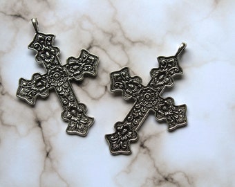 May include: Two silver ornate cross charms with intricate floral designs.