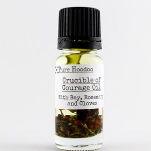 May include: A small glass bottle with a black lid filled with a yellow liquid and herbs. The label reads "Pure Hoodoo Crucible of Courage Oil With Bay, Rosemary and Cloves."
