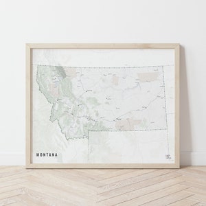 May include: A framed map of Montana with a light green and beige color scheme. The map shows the state's major cities, towns, and roads. The frame is made of wood and has a light brown finish. The text "MONTANA" is printed in black at the bottom of the map.