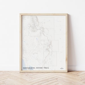 May include: A framed map of the Continental Divide Trail, a long-distance hiking trail in the United States. The map is printed in black and white and shows the trail's route through the Rocky Mountains. The map is framed in a light wood frame.