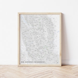 May include: A framed map of the Bob Marshall Wilderness in Montana. The map is printed in black and white and shows the location of trails, lakes, and other points of interest.