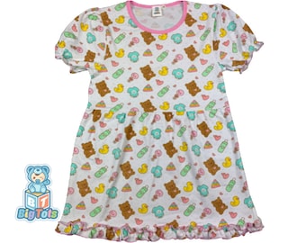 May include: White cotton dress with short sleeves and a ruffled hem. The dress has a pink trim around the neckline and features a print of brown bears, yellow ducks, blue pacifiers, and green baby bottles.