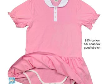 May include: Pink baby dress with a white collar and short, ruffled sleeves. The dress has a white placket with three buttons and a skirted bottom. The text on the image says "95% cotton 5% spandex good stretch". The Big Tots logo is in the bottom left corner.