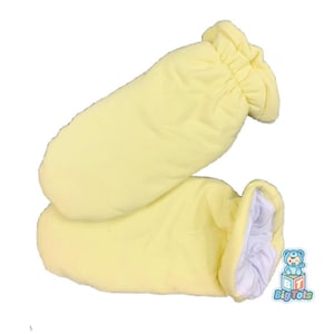 May include: A pair of soft, yellow baby mittens. The mittens are made of a plush material and have a gathered cuff. The interior of the mittens is white. The Big Tots logo is visible in the bottom right corner.