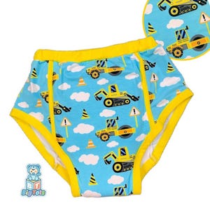 May include: Blue training pants with a construction vehicle pattern. The pants have yellow trim and a repeating pattern of yellow construction vehicles, clouds, traffic cones, and warning signs. The Big Tots logo is visible in the lower left corner.