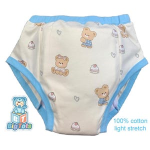 May include: Cream-coloured baby training pants with a light blue trim and elastic waistband. The pants feature a repeating pattern of cartoon teddy bears, cakes, and hearts. The text "100% cotton light stretch" is printed on the lower right.
