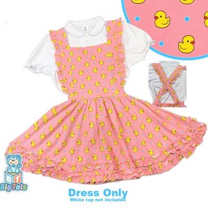 May include: A pink pinafore dress featuring a repeating pattern of yellow rubber ducks and small blue dots. The dress has ruffled shoulder straps and a ruffled hemline. A separate inset shows the back with crossed straps. Text reads: Dress Only.