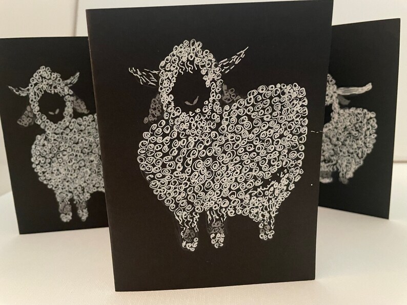 May include: Three black cards with white illustrations of sheep. Each sheep is drawn with a curly, textured wool pattern.