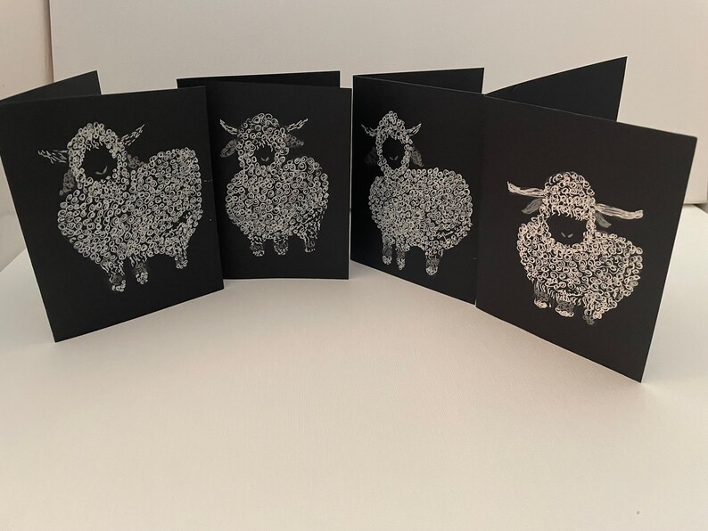 May include: Set of four black greeting cards with white illustrations of sheep. Each card features a different sheep design.
