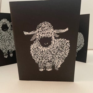 May include: Three black cards with white illustrations of sheep. The sheep are drawn with a swirling, curly pattern.