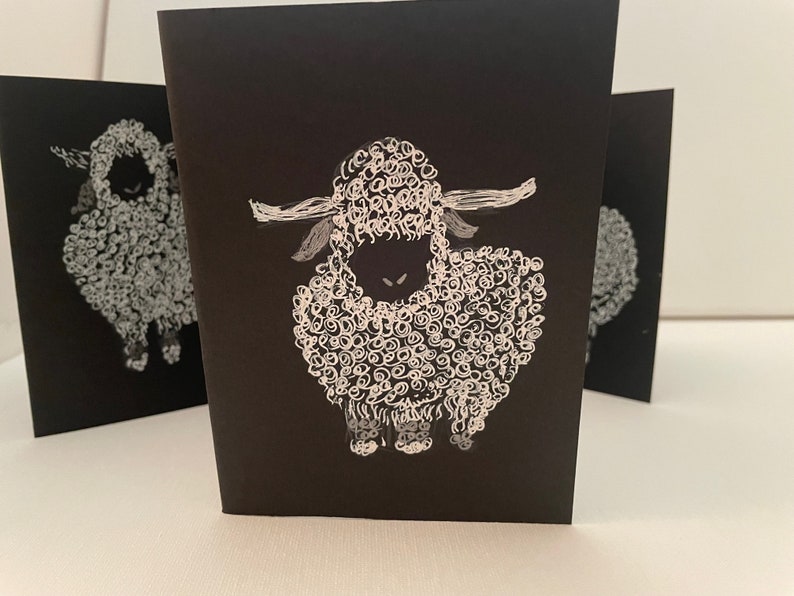 May include: Three black cards with white illustrations of sheep. The sheep are drawn with a swirling, curly pattern.