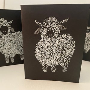May include: Three black cards with white illustrations of sheep. Each sheep is drawn with a fluffy, curly coat and a simple face.