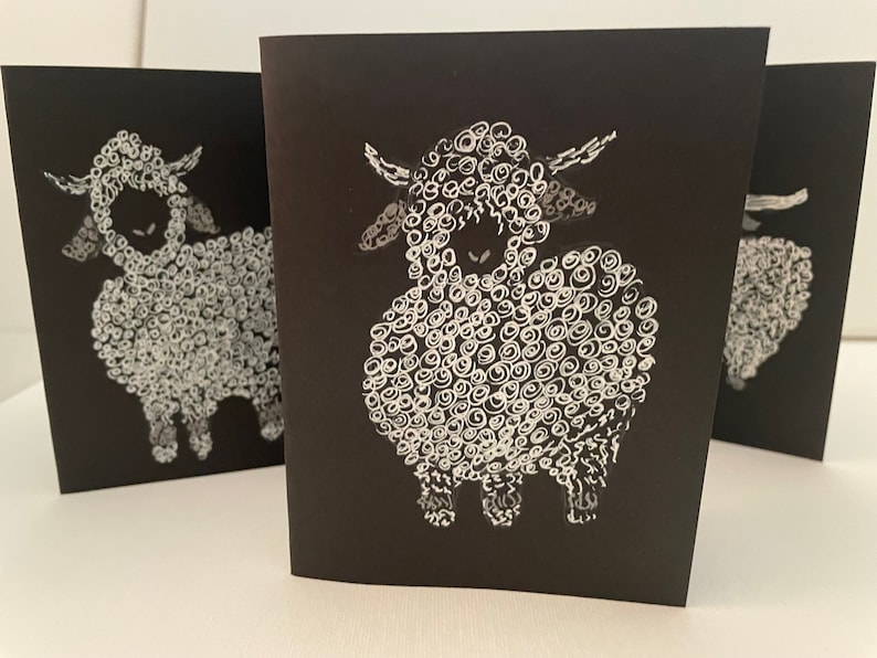 May include: Three black cards with white illustrations of sheep. Each sheep is drawn with a fluffy, curly coat and a simple face.