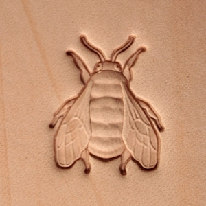 May include: A close-up of a leather stamp featuring a detailed design of a bee. The bee is carved into the leather and has a realistic appearance.