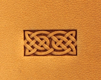 May include: A rectangular leather stamp with a Celtic knot design. The stamp features a series of interwoven loops and lines, creating a symmetrical pattern. The background is a textured, tan leather surface.