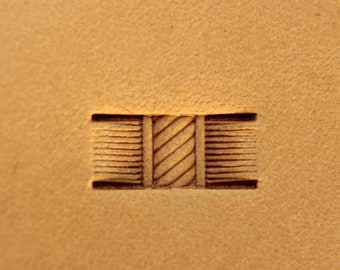 May include: A close-up of a leather crafting tool with a detailed design. The tool features a rectangular shape with a central diagonal pattern and parallel lines on either side, all in a dark brown color, pressed into the tan leather.