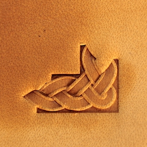 Może przedstawiać: Brązowa skórzana powierzchnia z rzeźbionym wzorem celtyckiego węzła w rogu.