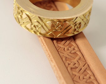 May include: A gold metal stamp with a Celtic knot design. The stamp is being used to create a pattern on a piece of leather.