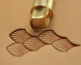 May include: A close-up of a brass leather stamping tool with a fan-shaped design. The tool is being used to create a pattern on a piece of leather.