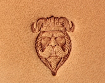 Op de afbeelding: Een leren stempel met een gedetailleerd ontwerp van een gezicht van een Viking-krijger met een gehelmde helm.