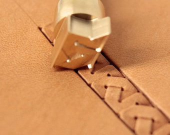 May include: A close-up of a leatherworking tool being used to create a decorative stitch on a piece of brown leather. The tool is made of brass and has a sharp point. The leather is being stitched with a braided pattern.