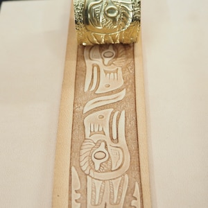 Puede incluir: Primer plano de una tira de cuero con un patrón decorativo en relieve. Se está utilizando un sello de latón para crear el patrón.
