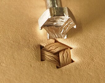 May include: A close-up of a metal leather stamping tool with a woven design. The tool is being pressed into a piece of leather, creating an impression of the woven design.