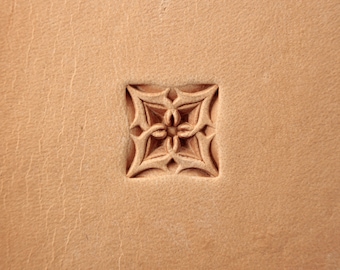 May include: A close-up of a leather surface with a decorative, carved design in the center. The design is a square with a four-pointed star in the middle.