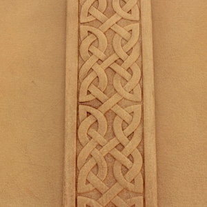Könnte beinhalten: Nahaufnahme einer braunen Lederoberfläche mit einem detaillierten, in die Oberfläche geschnitzten keltischen Knotendesign.