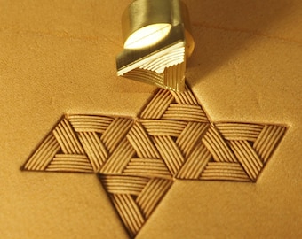 Può includere: Uno strumento di stampaggio in pelle in ottone con un design triangolare. Lo strumento viene utilizzato per creare uno schema intrecciato sulla pelle.