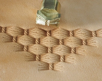 May include: A close-up of a leather stamping tool with a brass head and a metal handle. The tool is used to create a decorative pattern on leather. The pattern is a series of interlacing lines that create a woven effect.