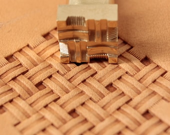 May include: A close-up of a brass leather stamping tool with a geometric pattern. The tool is resting on a piece of leather with a woven pattern.