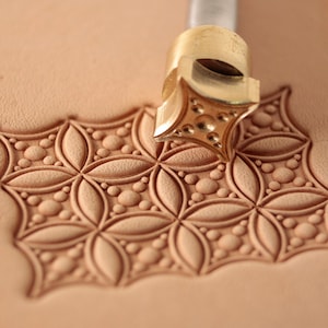 Puede incluir: Una herramienta de estampado de cuero de latón con un diseño en forma de estrella. La herramienta se utiliza para crear un patrón en un trozo de cuero.