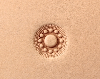 Può includere: Un primo piano di uno strumento di stampaggio in pelle con un design circolare che presenta un cerchio centrale circondato da un anello di cerchi più piccoli.