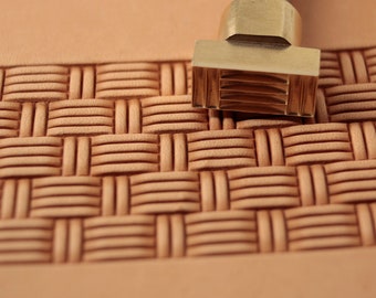 May include: A brass leather stamping tool with a woven pattern design. The tool is on a piece of leather that has been stamped with the same pattern.