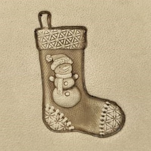 May include: A brown leather stocking with a white snowflake pattern and a snowman design. The snowman is wearing a hat and scarf.