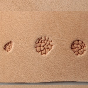 Op de afbeelding: Close-up van een lichtbruin lederen oppervlak met drie geëmbosseerde ontwerpen. De ontwerpen zijn rond en hebben een textuurpatroon van kleine, verhoogde cirkels.