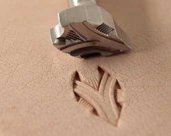 May include: A close-up of a leather stamping tool with a detailed design. The tool is being used to create a decorative pattern on a piece of leather.