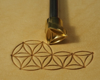 Könnte beinhalten: Ein Lederprägewerkzeug aus Messing mit einem dreieckigen Design. Das Werkzeug wird verwendet, um ein Lebensblumenmuster auf Leder zu erstellen.