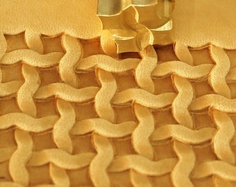 May include: A close-up of a leather stamping tool with a woven pattern. The tool is made of brass and has a star-shaped design. The tool is being used to create a woven pattern on a piece of leather.