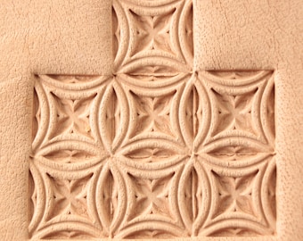 Può includere: Primo piano di una superficie in pelle con un motivo decorativo di cerchi e quadrati sovrapposti. Il motivo è in rilievo sulla pelle, creando un design rialzato.
