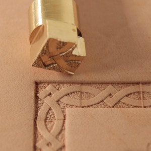 May include: A brass leather stamping tool with a Celtic knot design. The tool is used to create decorative patterns on leather.