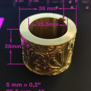 May include: A gold-coloured, cylindrical object with ornate floral and leaf patterns. The object has a key slot and measures 38 mm in diameter, 28 mm in height, and 25.5 mm in internal diameter. The key slot is 5 mm.