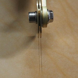 Puede incluir: Primer plano de una herramienta de metal con mango amarillo y tuerca plateada. La herramienta tiene dos cuchillas finas y transparentes alineadas verticalmente.