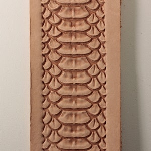 Może przedstawiać: Zbliżenie na jasnobrązowy pasek skórzany z wytłoczonym wzorem skóry węża.